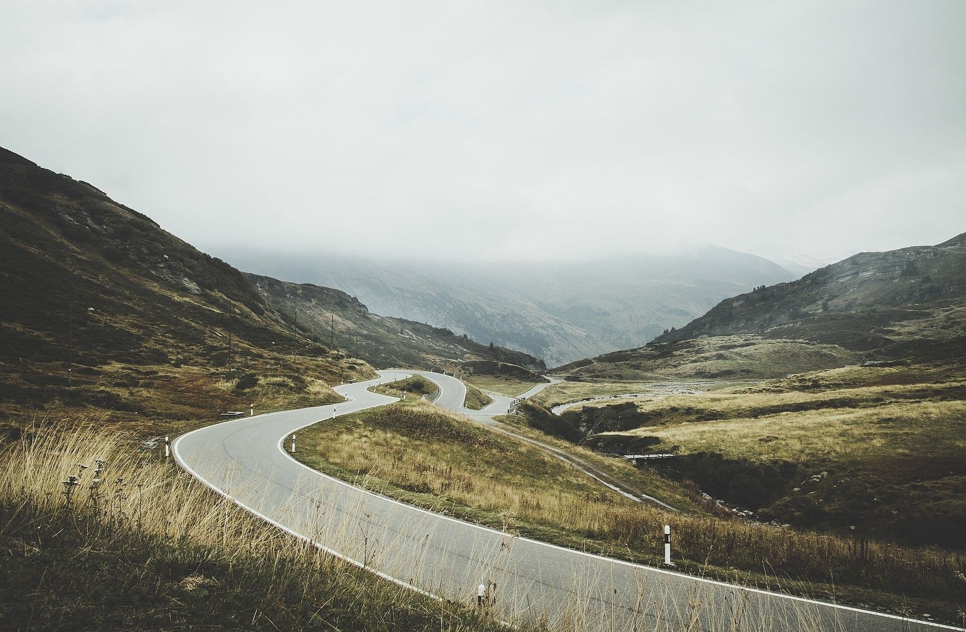 A road winding up a mountain valley towards cloud.